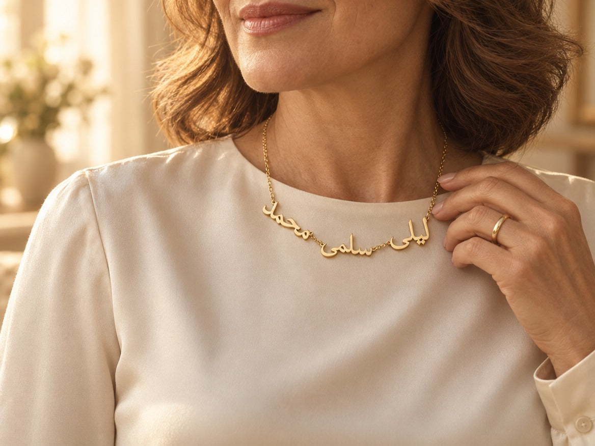 Woman wearing a custom Arabic multiple name necklace in 18K gold plating with three names, ليلى, سلمى and محمد, over a cream blouse