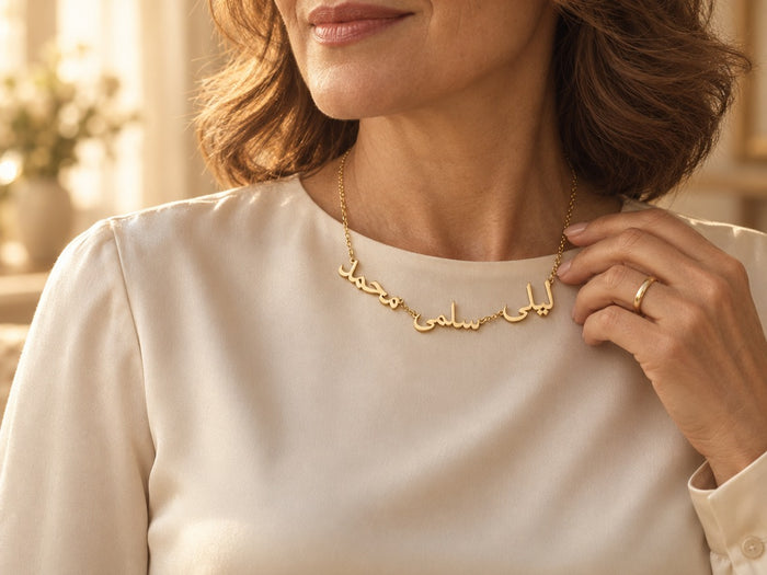 Woman wearing a custom Arabic multiple name necklace in 18K gold plating with three names, ليلى, سلمى and محمد, over a cream blouse