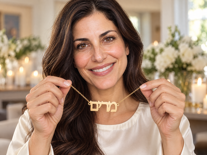 Smiling woman holding up a gold Hebrew name necklace reading מרים as a Bat Mitzvah gift