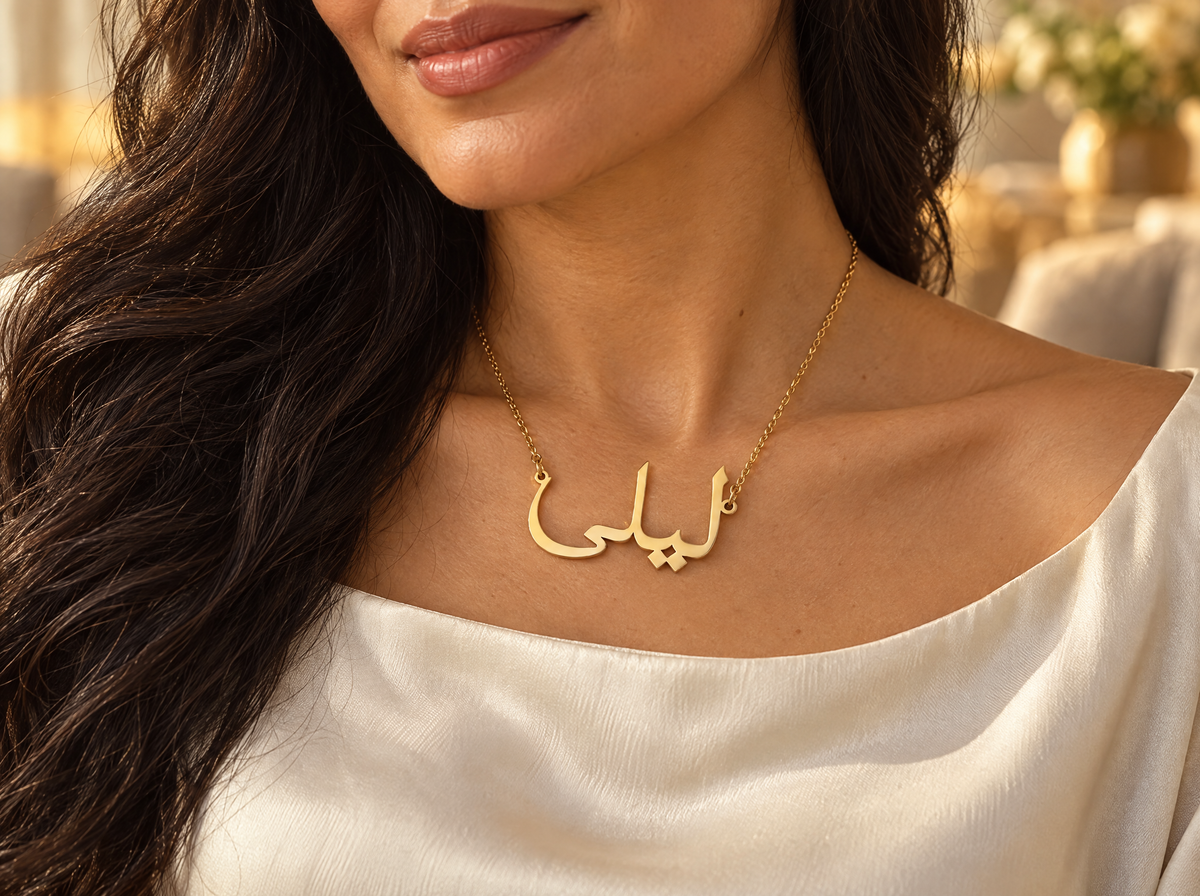 Woman wearing a gold Arabic name necklace reading ليلى (Layla) over a cream silk blouse