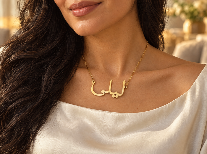 Woman wearing a gold Arabic name necklace reading ليلى (Layla) over a cream silk blouse