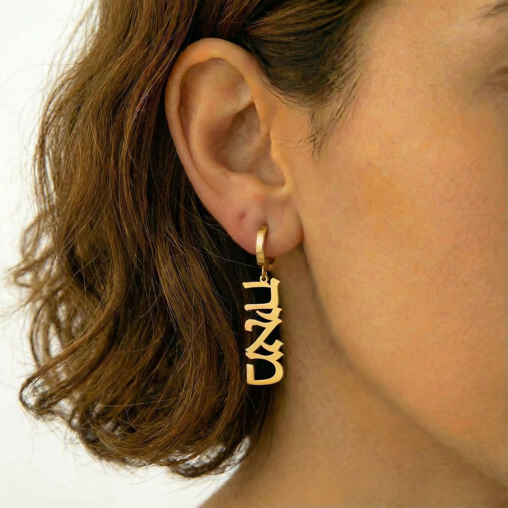 Personalized name drop earrings in Hebrew in gold finish worn on ear, side profile view