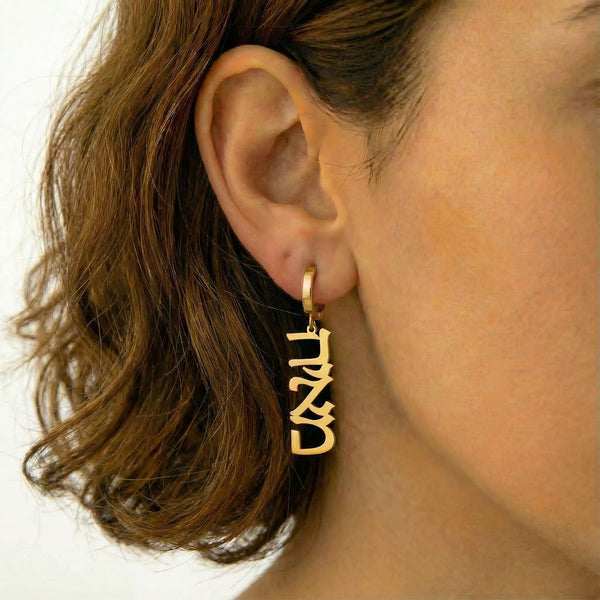 Personalized name drop earrings in Hebrew in gold finish worn on ear, side profile view