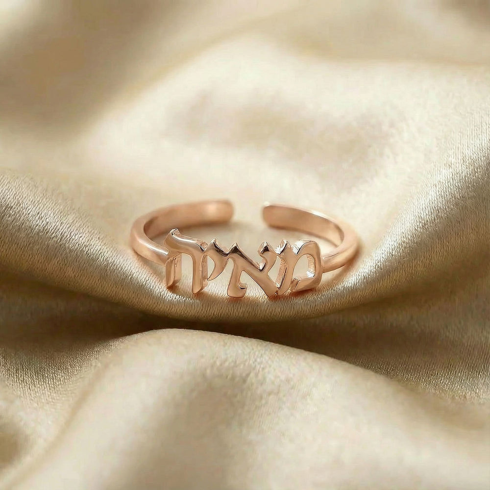 Personalized name ring in Hebrew, one-size in rose gold finish on beige silk fabric