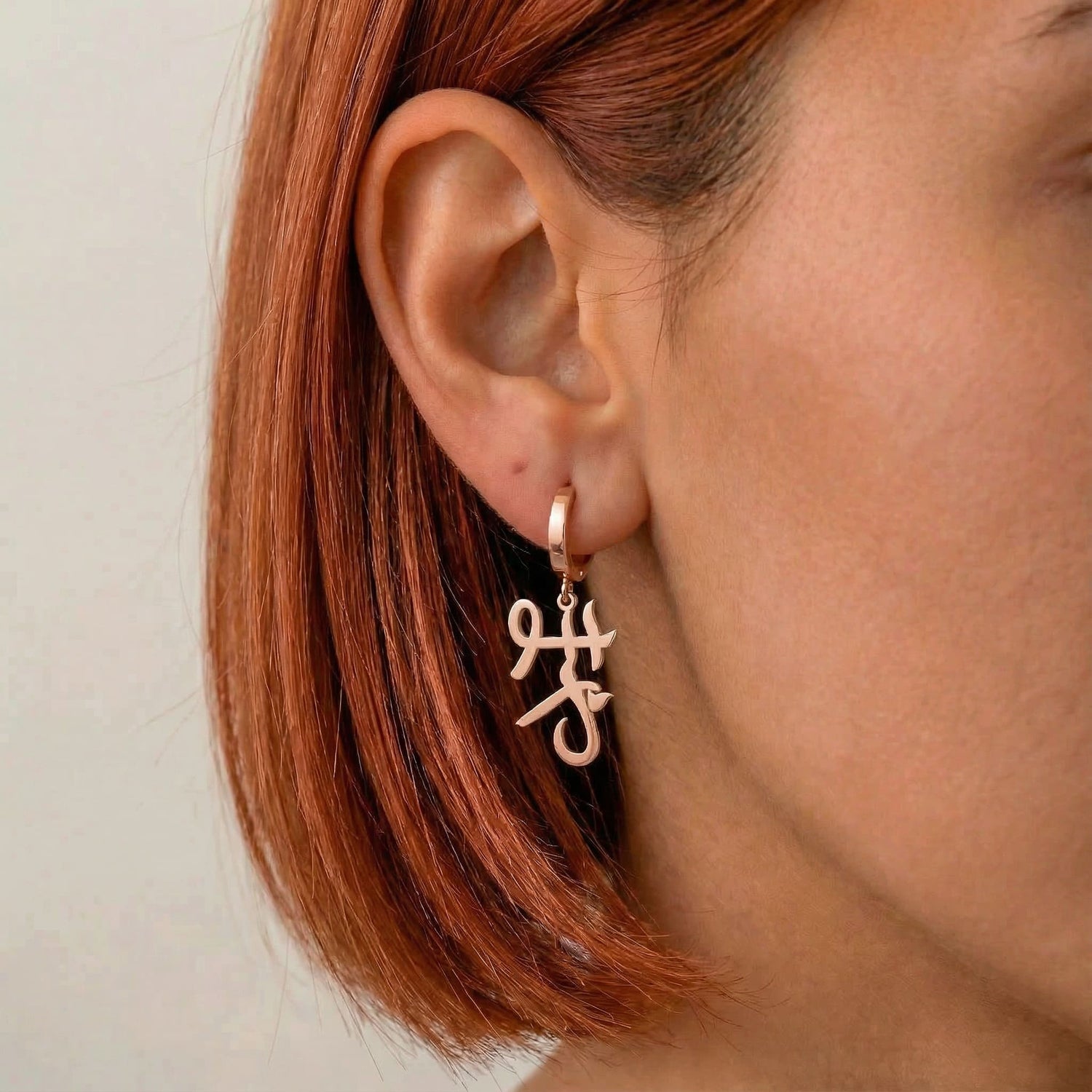 Personalized name drop earrings in Japanese in rose gold finish worn on ear, side profile view