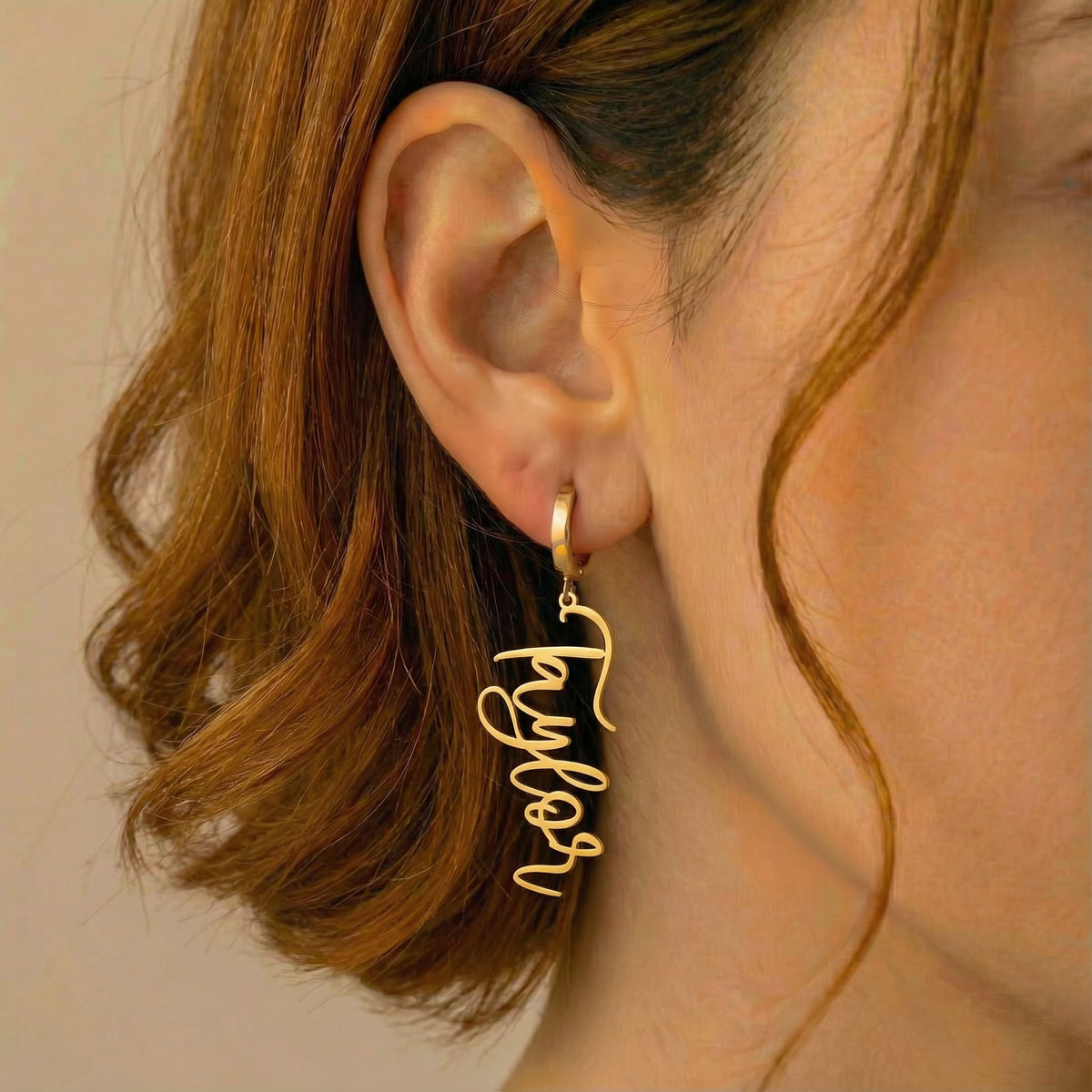 Personalized name drop earrings in gold finish worn on ear, side profile view