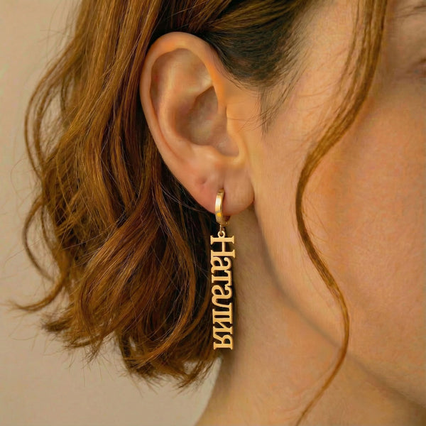Personalized name drop earrings in Cyrillic in gold finish worn on ear, side profile view