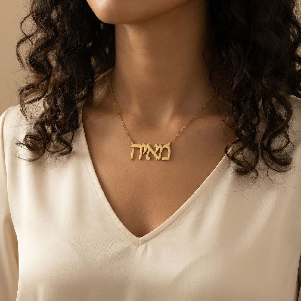 Gold Hebrew script name necklace reading מאיה worn on woman’s neck in lifestyle image