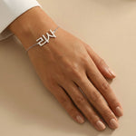 Silver Korean name bracelet displayed on a tanned wrist with clean unpolished nails, styled on a smooth cream background under natural daylight.