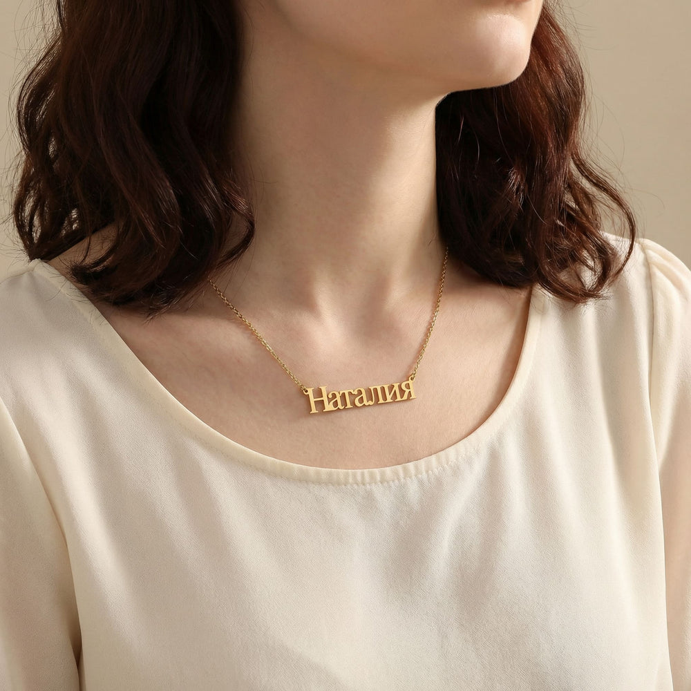 Gold Cyrillic script name necklace reading Наталия worn on woman’s neck