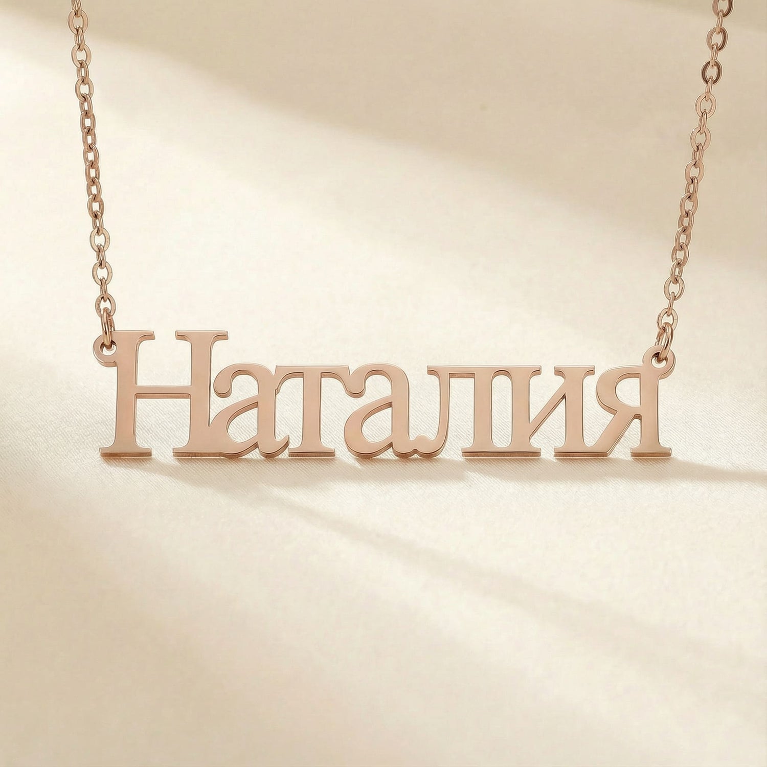 Personalized name necklace in Cyrillic in rose gold finish on beige silk fabric