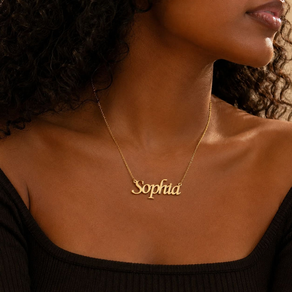 Dark-skinned curly-haired woman wearing a gold 'Sophia' custom name necklace with a black off-shoulder top