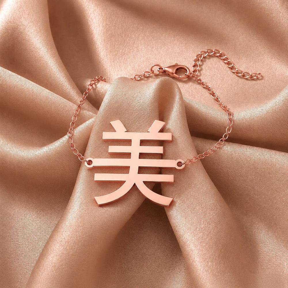 Rose gold necklace with a Kanji character pendant meaning "beauty" on a beige fabric background