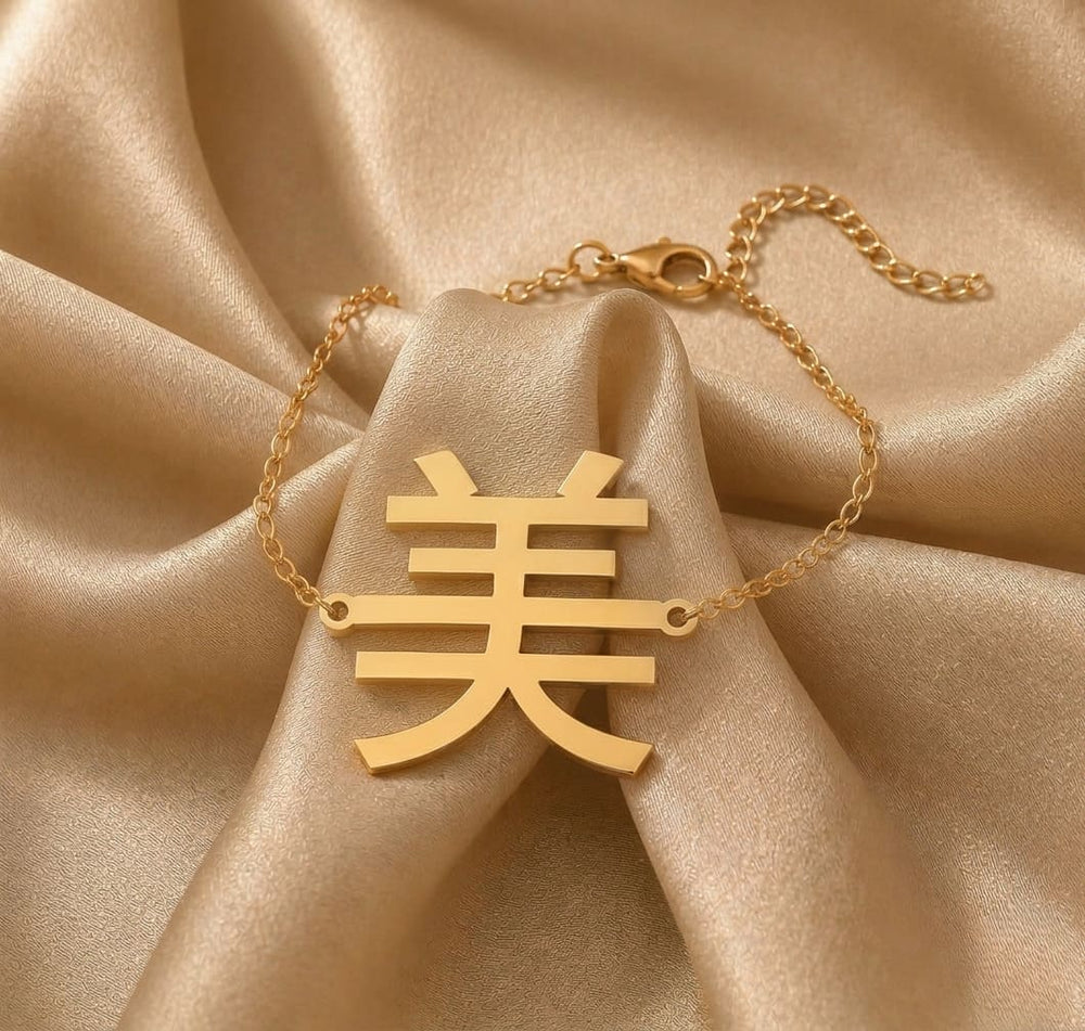 Gold necklace with a Kanji character pendant meaning "beauty" on beige fabric