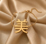 Gold necklace with a Kanji character pendant meaning "beauty" on beige fabric