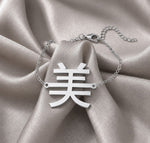 Silver necklace with a Kanji pendant meaning "beauty" on a beige fabric background