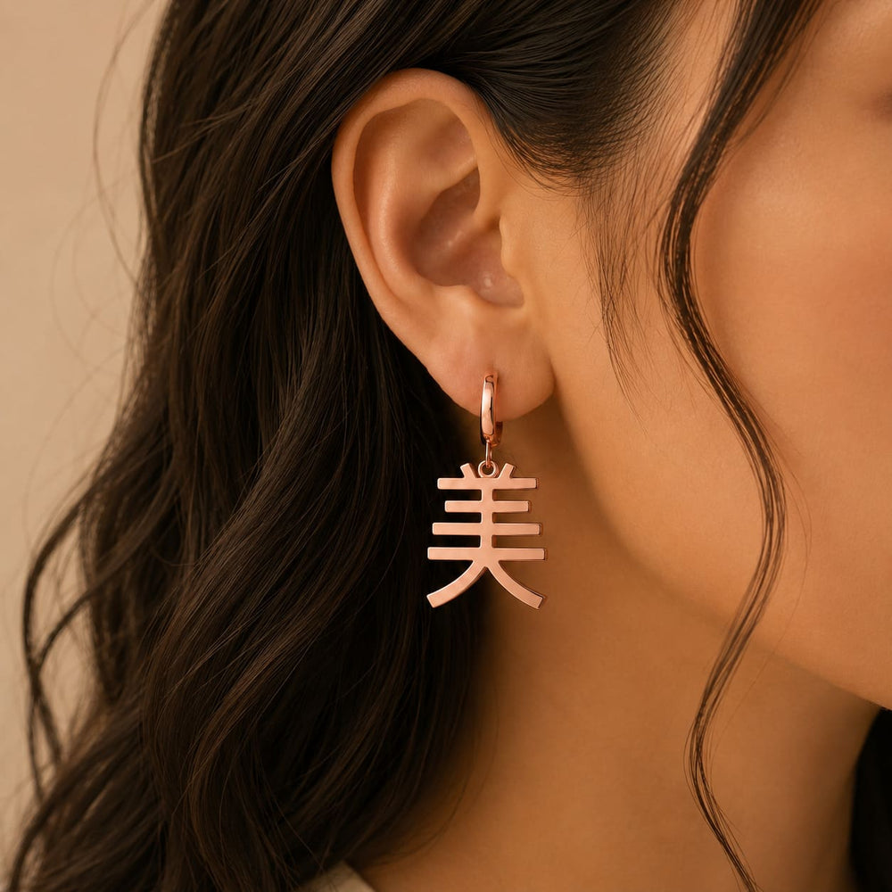 Rose gold earrings with a Kanji character meaning "beauty" worn by a person with wavy hair.