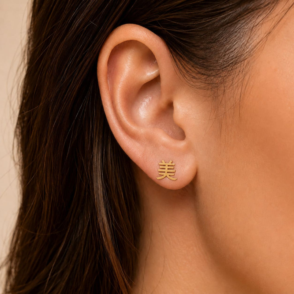 Gold earring with a Kanji character meaning "beauty" worn by a person against a neutral background