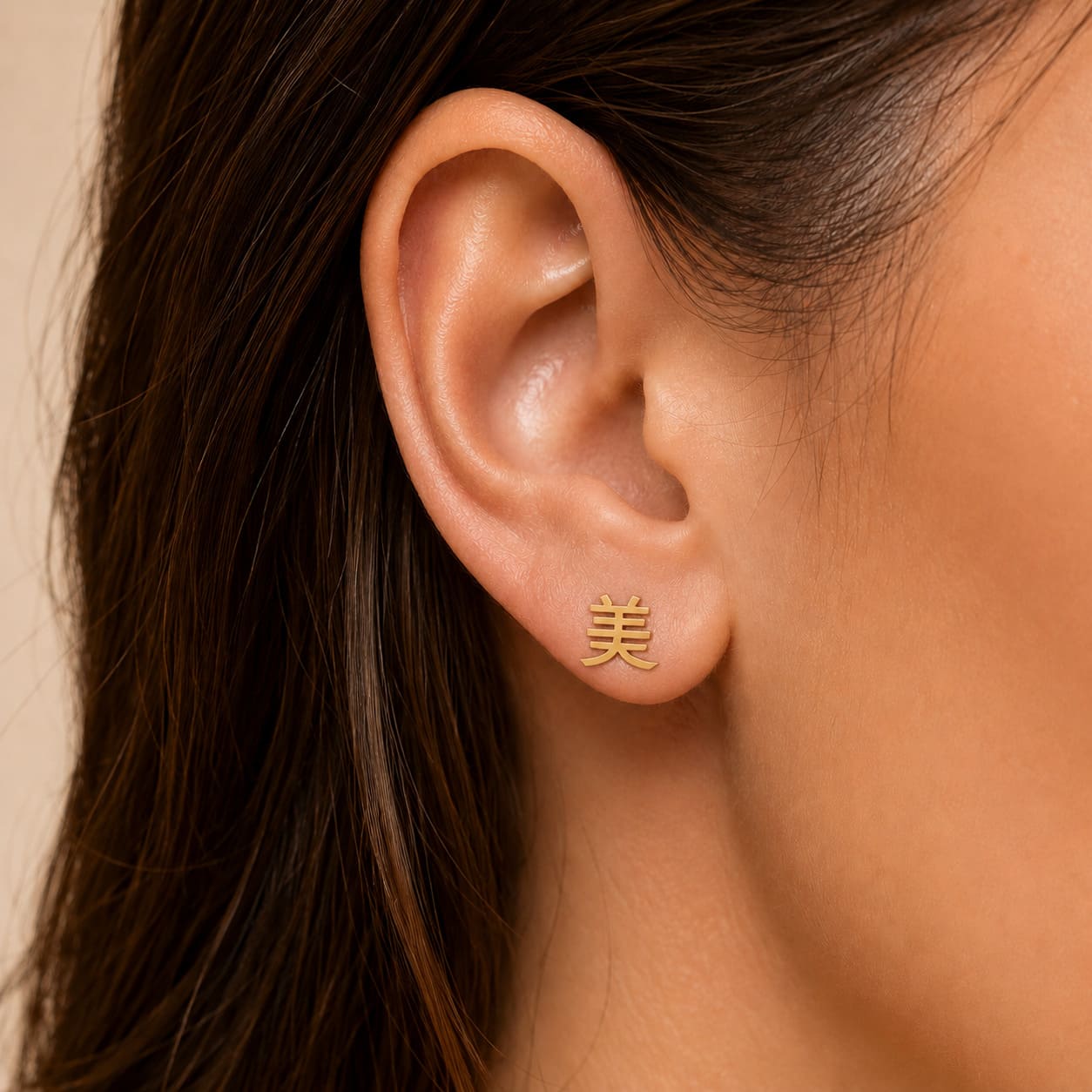 Gold earring with a Kanji character meaning "beauty" worn by a person against a neutral background