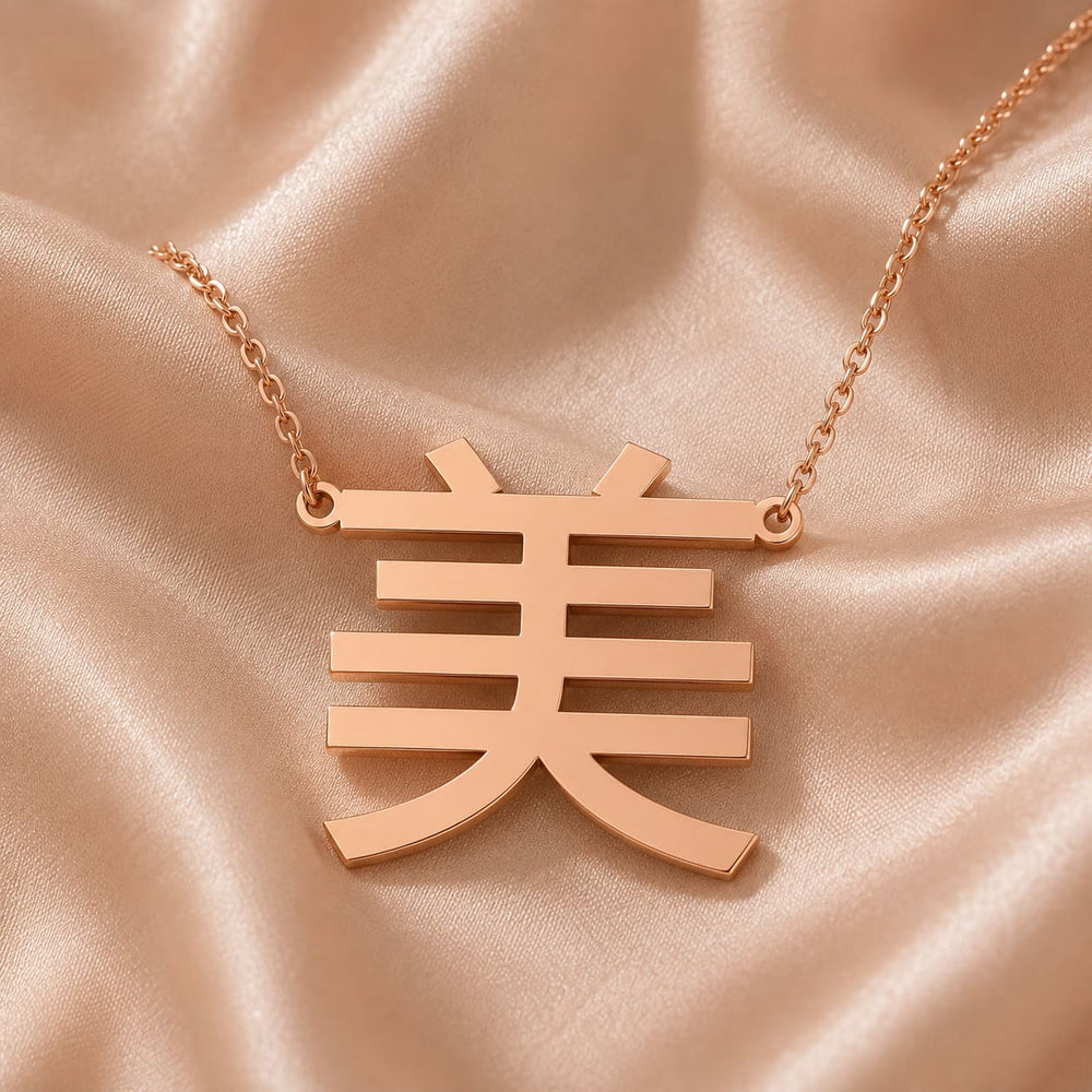 Rose gold necklace with a Kanji character  pendant meaning "beauty" on a pink satin background