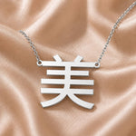 Silver necklace with a pendant featuring a Kanji character meaning "beauty" on a beige fabric background