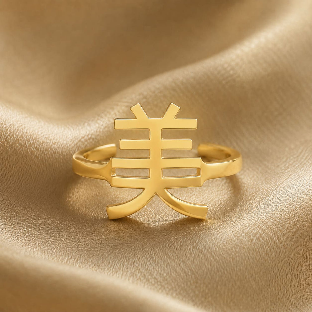 Gold ring with a Kanji character meaning "beauty" on a gold fabric background
