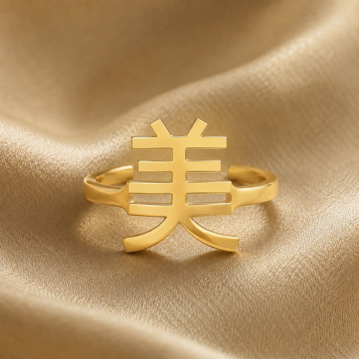 Gold ring with a Kanji character meaning "beauty" on a gold fabric background