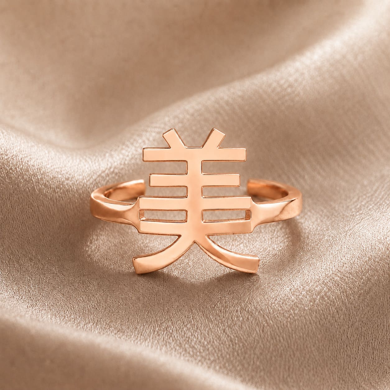 Rose gold ring with a Kanji character pendant meaning "beauty" on a beige fabric background