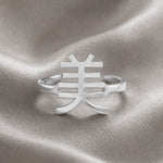 Silver ring with a Kanji character design meaning "beauty" on a textured silver background