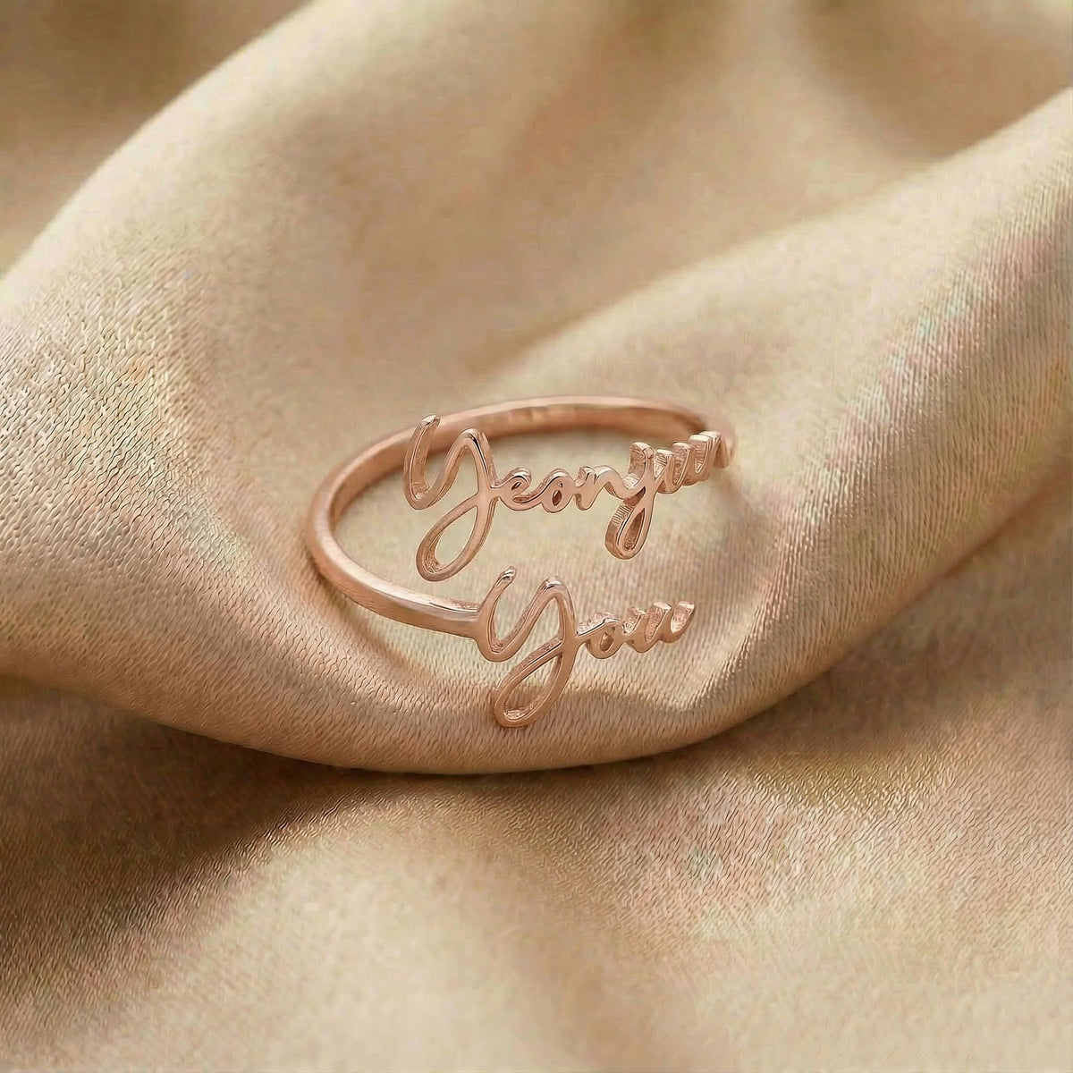 Personalized name ring, one-size in rose gold finish on beige silk fabric