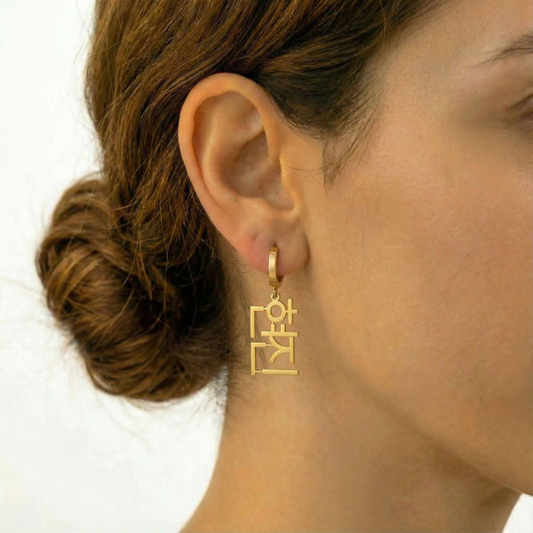 Personalized name drop earrings in Korean in gold finish worn on ear, side profile view