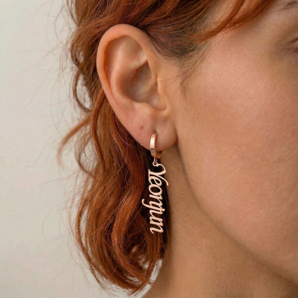 Personalized name drop earrings in rose gold finish worn on ear, side profile view