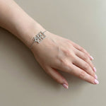 Silver Korean Hangul name bracelet worn on a fair toned wrist, shown on a relaxed hand with natural short nails against a soft beige background in natural light.