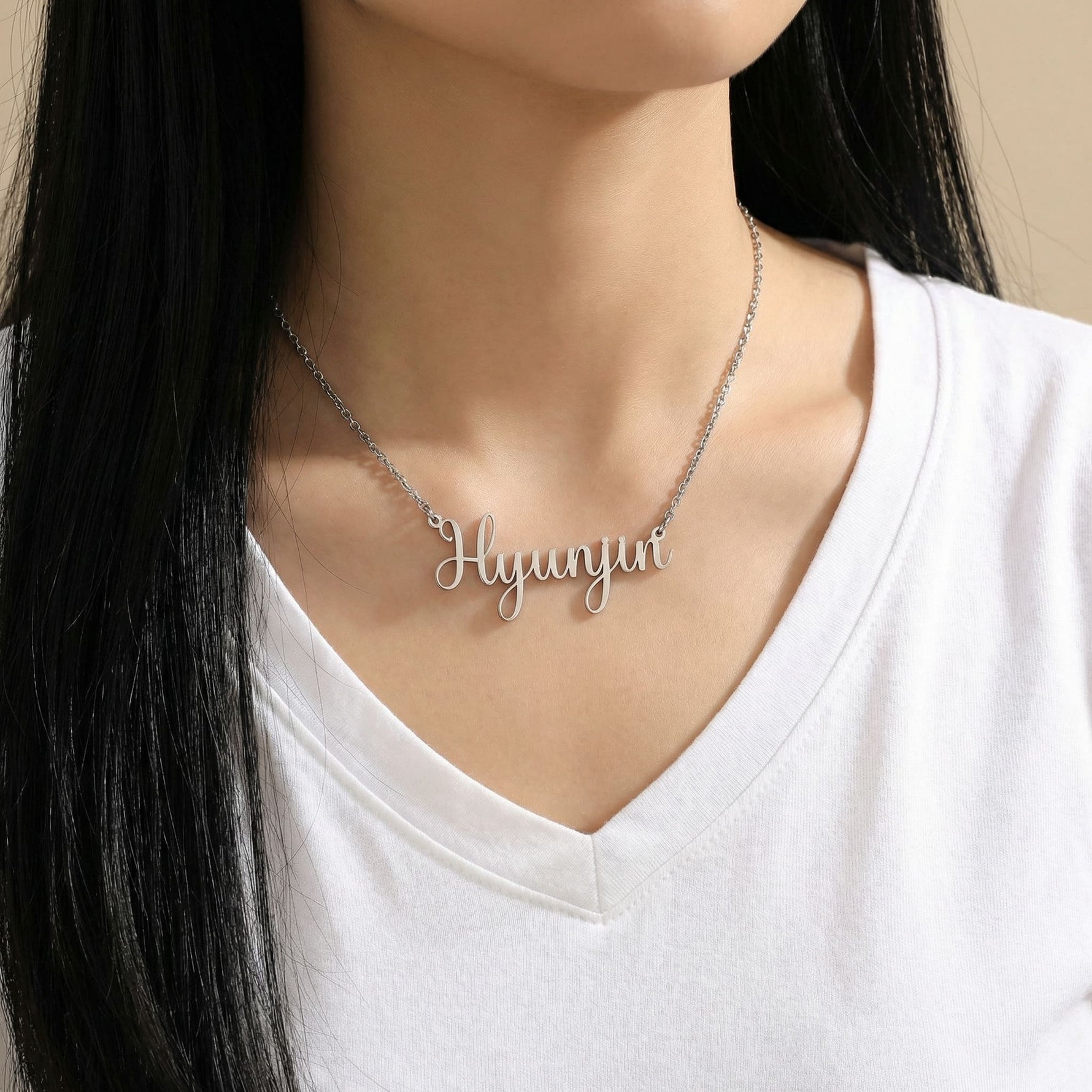 Silver Latin script K-pop idol name necklace reading Hyunjin worn on woman’s neck
