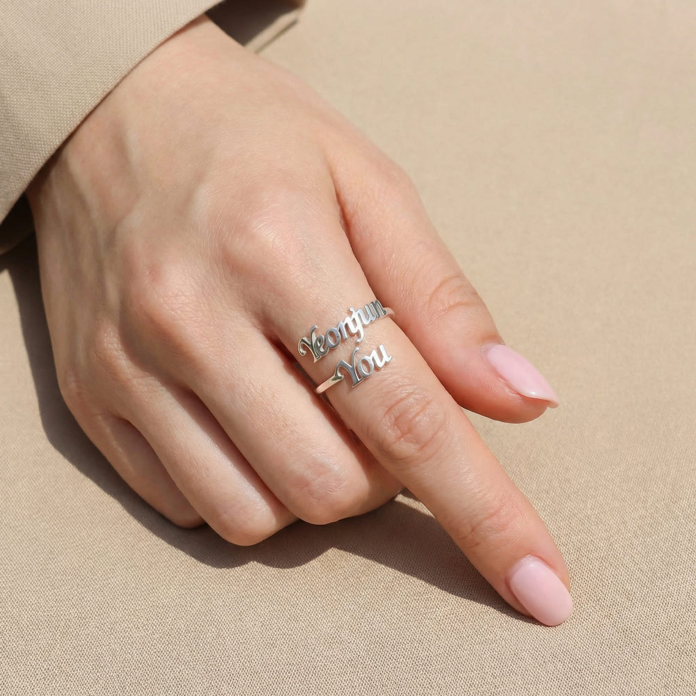 Woman's hand wearing a silver K-pop bias couple name ring featuring "Yeonjun" and "You" in two rows of cursive script on the index finger, casual pose with beige sleeve visible.