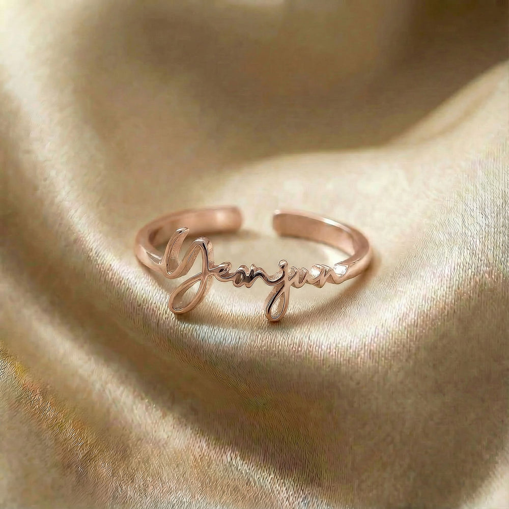 Personalized name ring, one-size in rose gold finish on beige silk fabric
