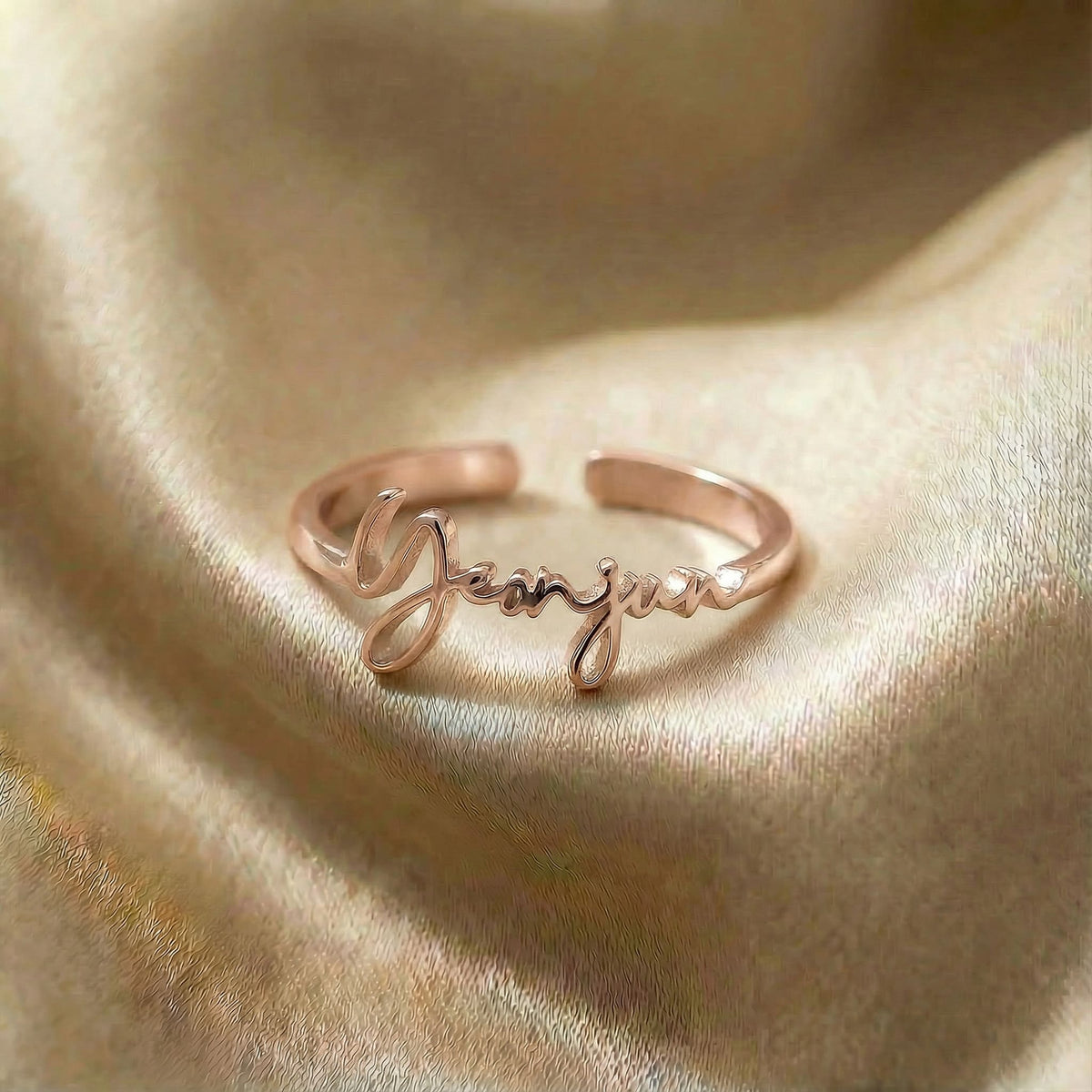 Personalized name ring, one-size in rose gold finish on beige silk fabric
