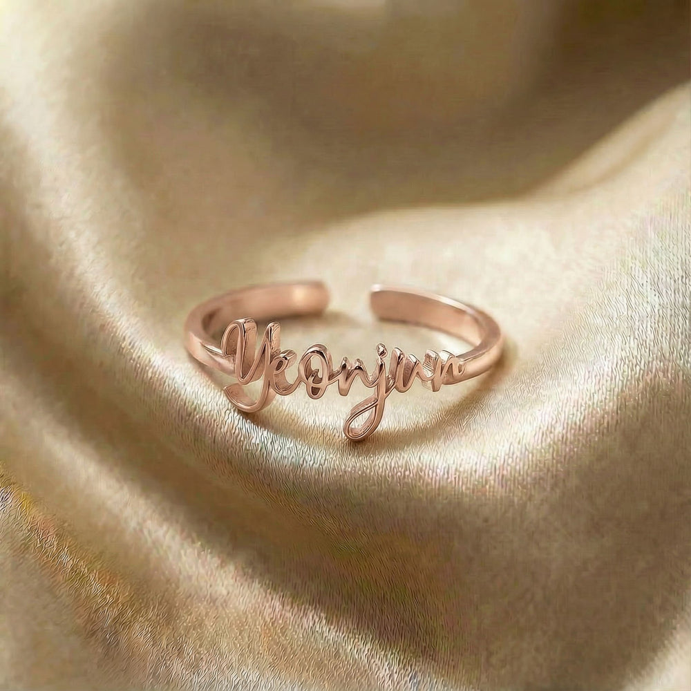 Personalized name ring, one-size in rose gold finish on beige silk fabric