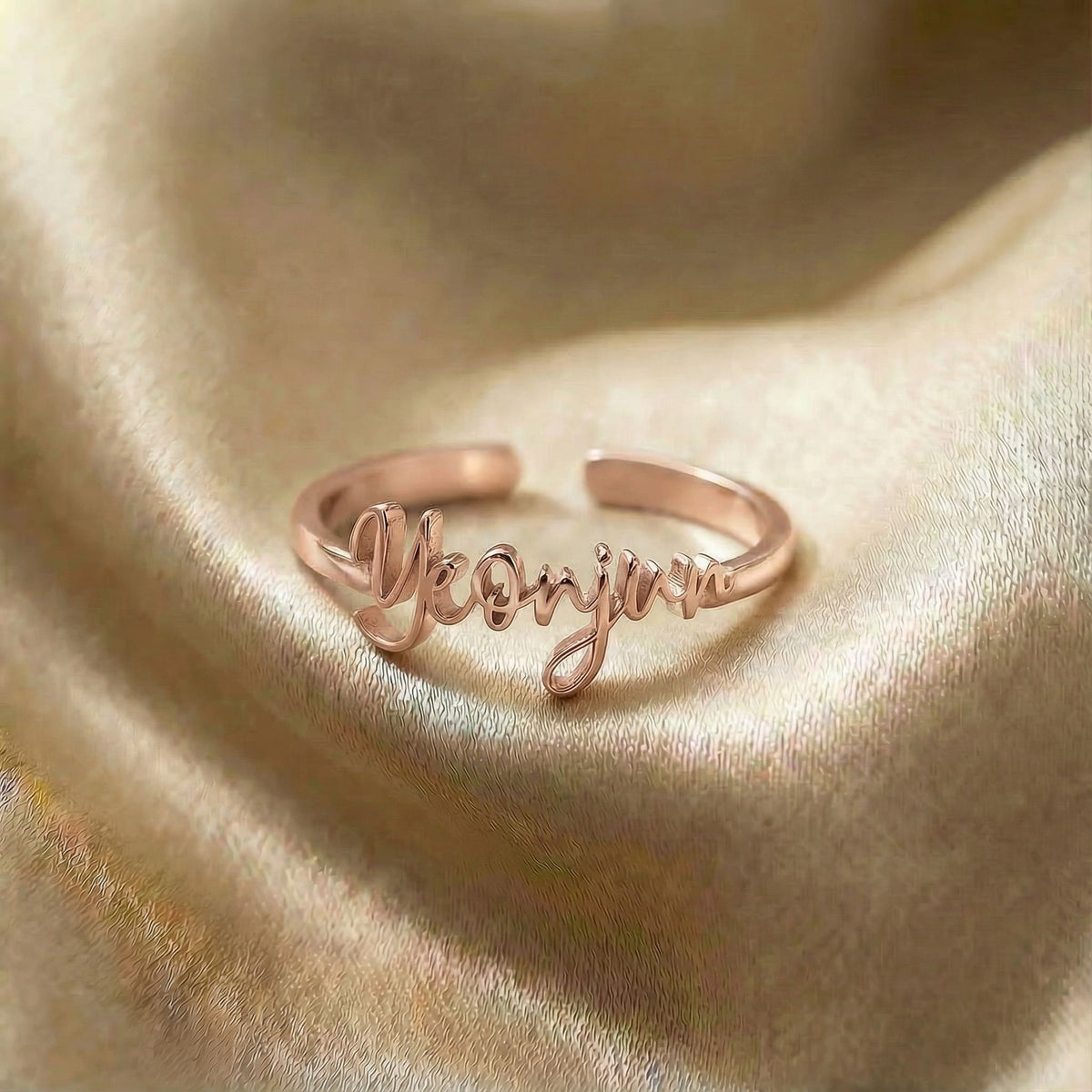 Personalized name ring, one-size in rose gold finish on beige silk fabric