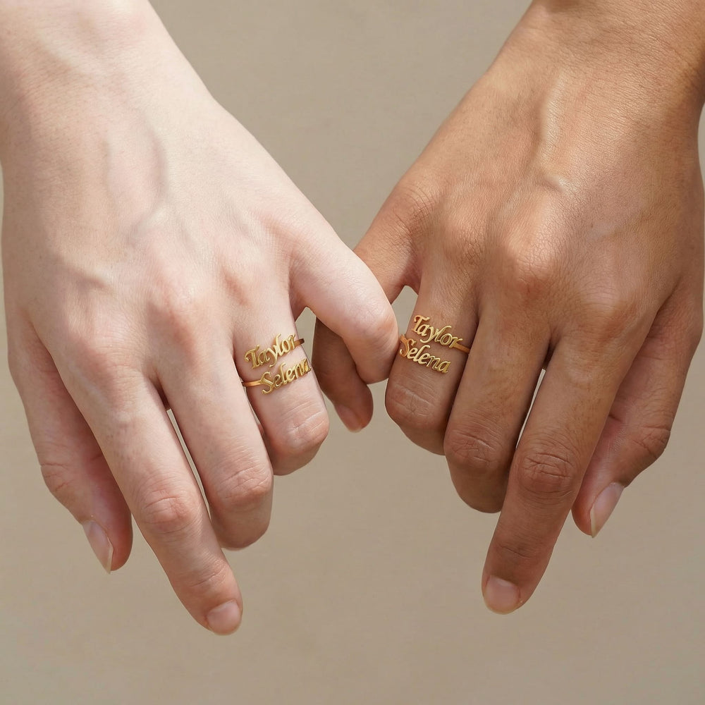 Two hands side by side each wearing matching gold best friends name rings with "Taylor" and "Selena" in cursive script, showing different skin tones in a friendship pose.