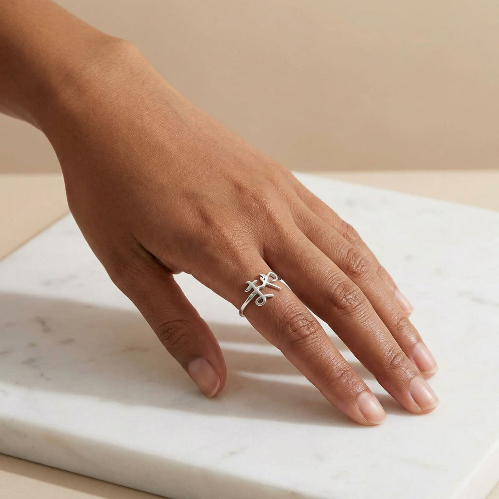 Woman's hand wearing a silver custom Japanese Hiragana name ring on the middle finger, hand resting elegantly on white marble surface with warm beige background.