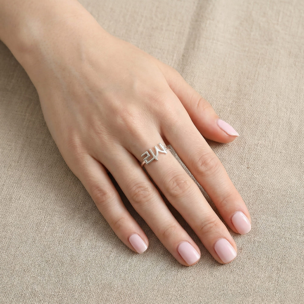 Woman's hand wearing a silver custom Korean Hangul name ring with "리사" (Lisa) on the middle finger, hand flat on beige linen fabric with soft pink nails.