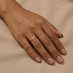 Woman's hand wearing a gold custom name ring with "Sophia" in cursive script on the middle finger, hand relaxed on beige satin fabric with nude nails.