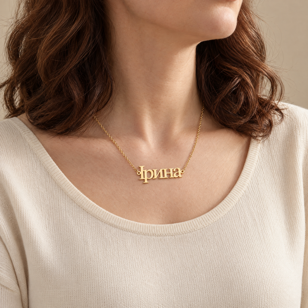 Woman wearing a personalized Ukrainian name necklace reading Ірина in 18K gold plating with a cream knit top