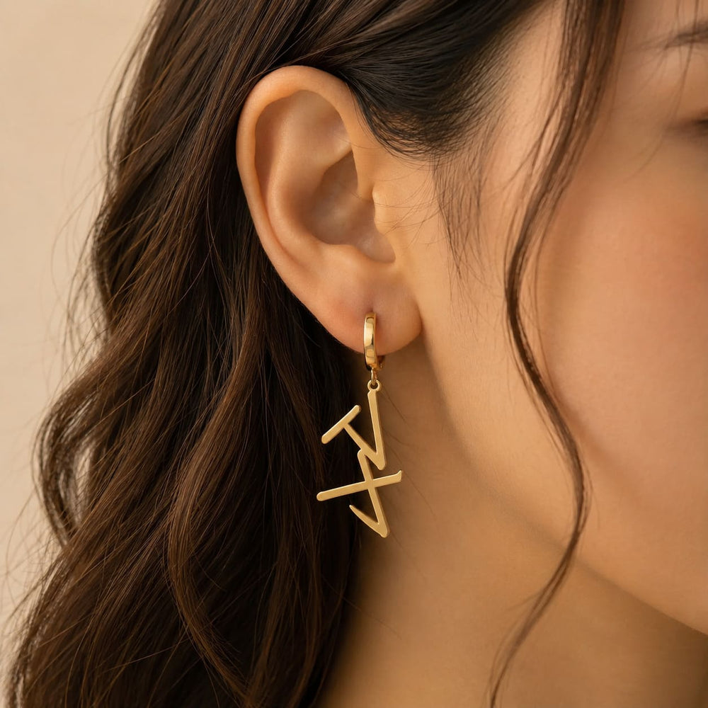 Gold drop earrings in Japanese Katakana meaning "Maya" worn by a person with wavy hair against a neutral background