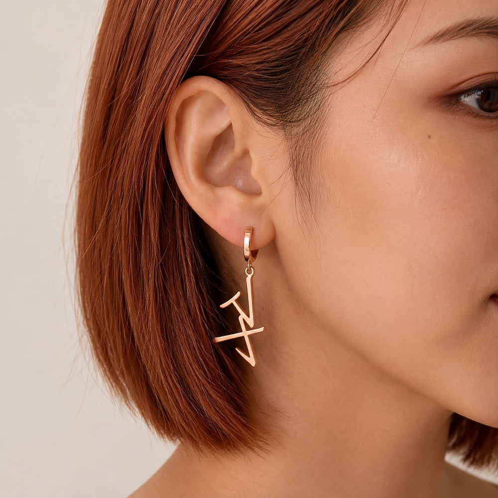 Rose gold drop earrings in Japanese Katakana meaning "Maya" worn by a woman with shorter hair against a neutral background