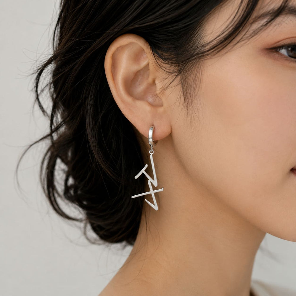 Silver drop earrings in Japanese Katakana meaning "Maya" worn by a woman against a neutral background