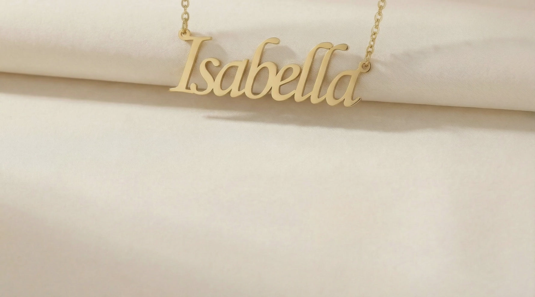 Isabella gold colored name necklace slow motion video with a silk cloth background